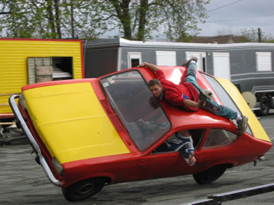A man on top of a car on two wheels