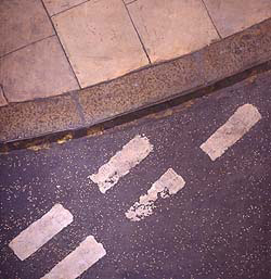 An incredibly detailed and realistic  of a street corner. At the top is a curve of kerb and pavement. At the bottom, tarmac with road markings in white paint