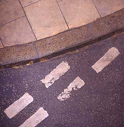 An incredibly detailed and realistic of a street corner. At the top is a curve of kerb and pavement. At the bottom, tarmac with road markings in white paint