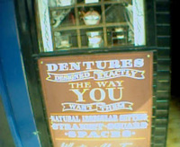 A sign advertising custom denture manufacture. While you wait, natch