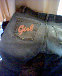 A pair of old jeans, with an iron-on patch that reads 'Girl' freshly applied to the left back pocket